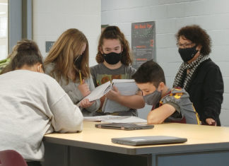 Picture of a woman standing behind a desk of students working together and looking over papers.
