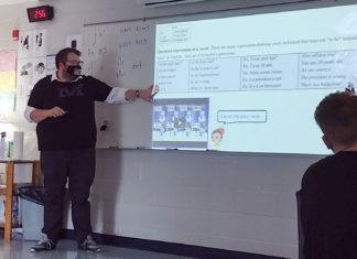 Picture of a man in a darkened room pointing toward a screen and talking to students.