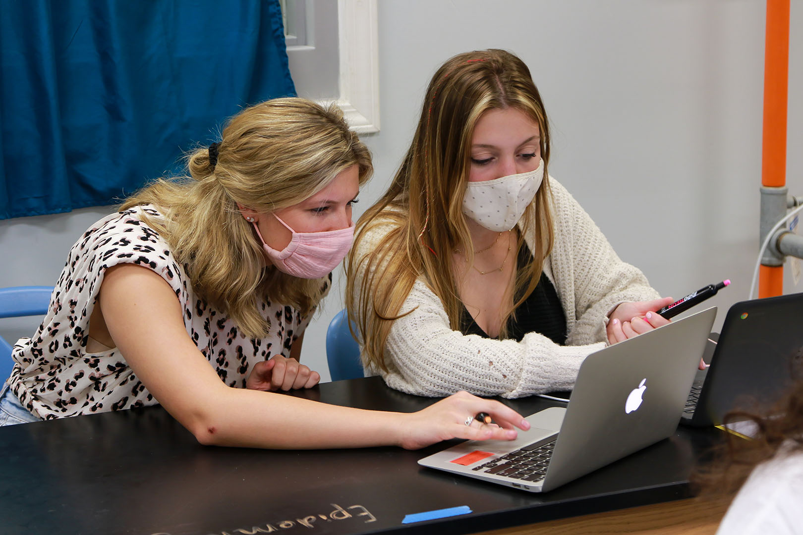 Picture of teacher and a student working on a computer together, both are wearing face masks.