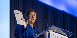 Picture of a woman holding a document, standing at a podium and speaking.