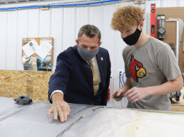 Picture of a man in a suit pointing to a section of airplane wing and talking to a student.