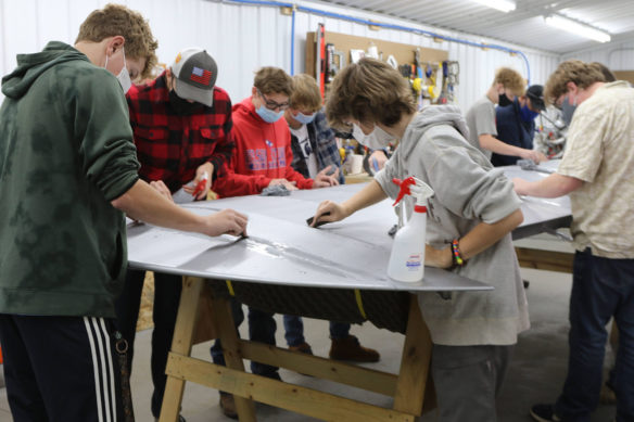 Picture of a group of students working on a airplane wing laying on sawhorses.