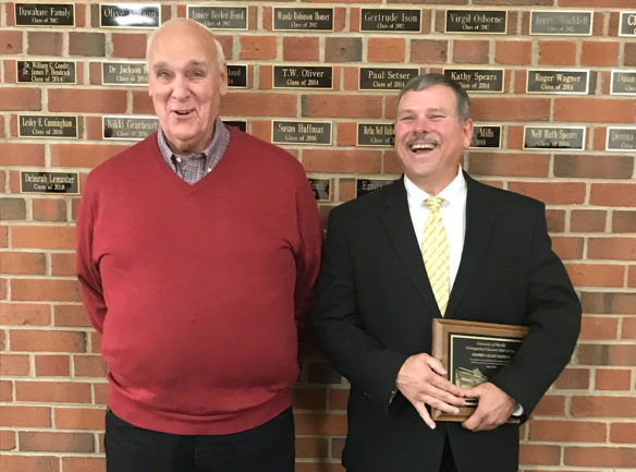 Picture of two men standing against a brick wall. One is talking and the other is laughing.