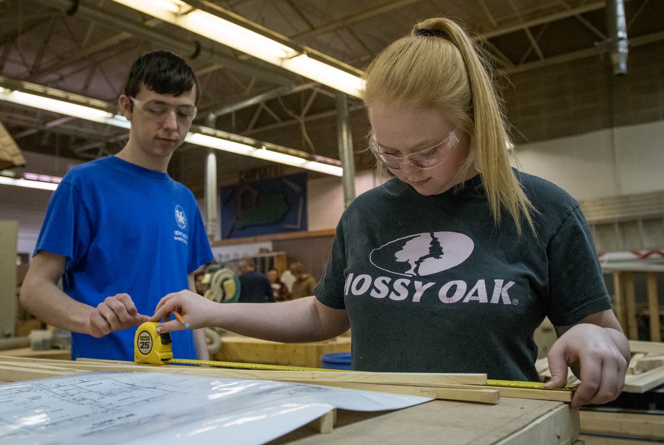 A picture of a high school boy and girls measuring pieces of wood in a shop.