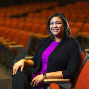 Picture of a woman sitting in a theater seat and smiling.