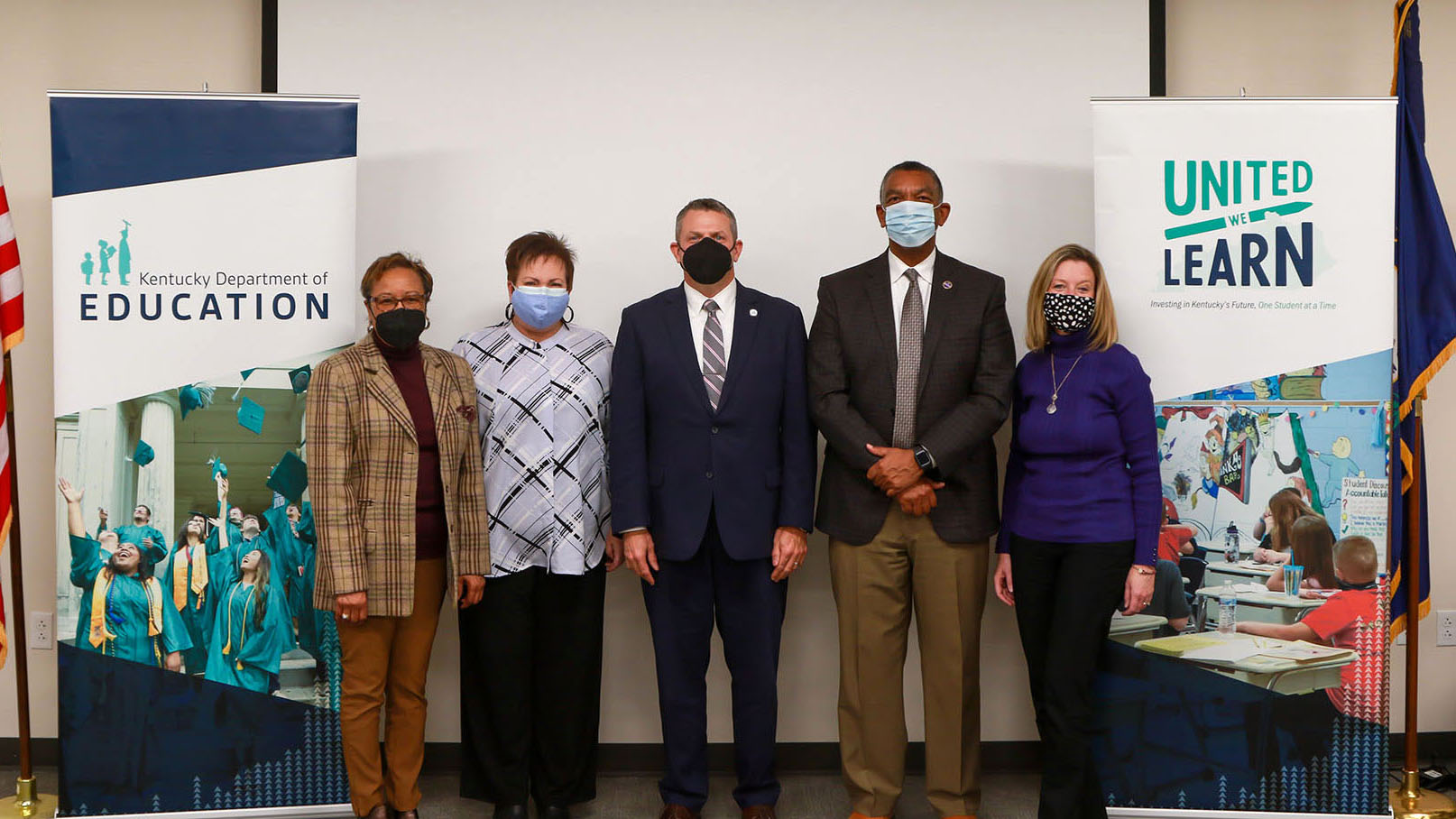 A picture of five people wearing face masks, standing between two posters reading the Kentucky Department of Education and United We Learn.