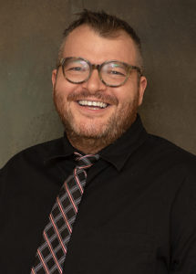 Picture of smiling man wearing glasses, a shirt and a tie.