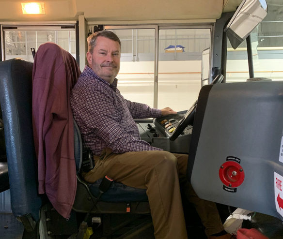 A man sits in the driver sear of a school bus smiling. 