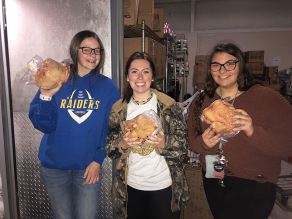 Three students stand holding cooked chicken meat. 