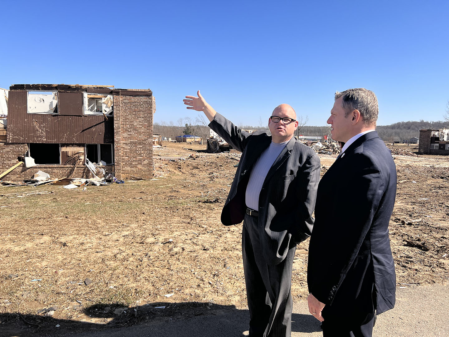 Picture of two men standing outside, with one man pointing toward a destroyed home.