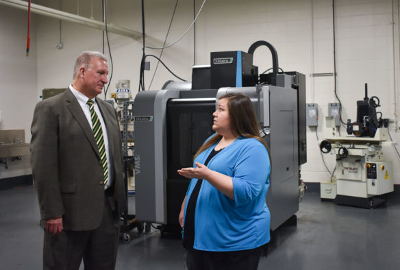 A man and a woman stand talking in front of machinery. 