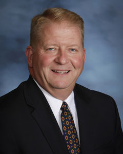 A headshot photo of a man in a suit smiling. 