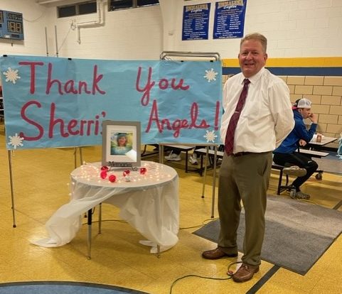 A man standing in front of a sign that reads "Thank You Sherri's Angels."