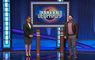 A woman and a man standing in front of a large screen that reads: Jeopardy!