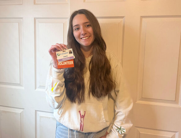 Picture of a smiling young woman holding up a badge that says "volunteer."