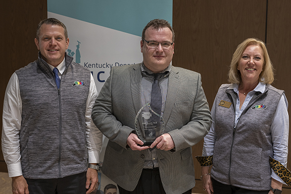 Picture of two men, one of them holding a glass award, and a woman standing together and smiling.