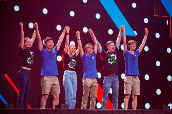 A group of students stand on a stage holding hands raised in the air.