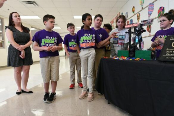 A group of students and their teacher look at a robotics display on a table. 