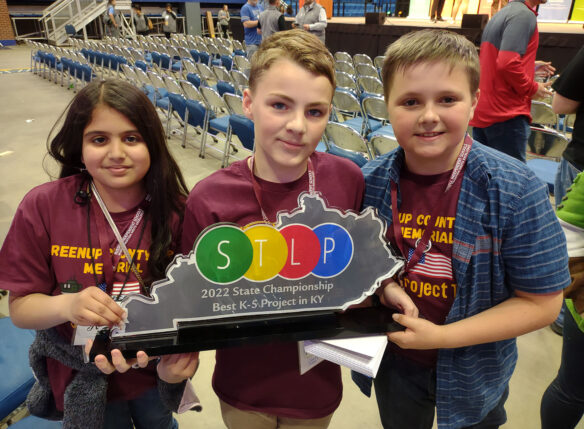 Three students hold a trophy in the shape of the state of Kentucky that reads: STLP, 2022 State Championship, Best K-5 Project in Kentucky.