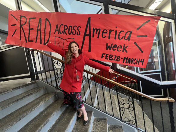 A woman stands in front of a banner that reads: "Read Across America Week"