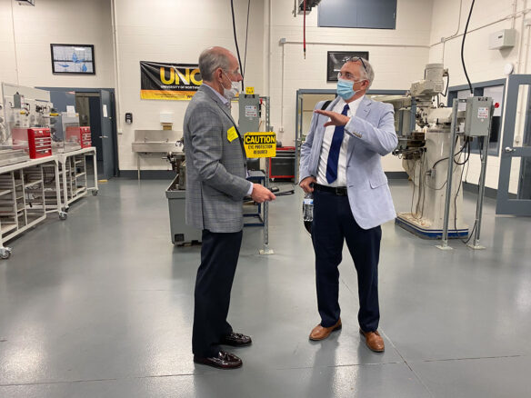 Two men standing in a room with different machinery behind them. 