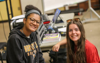 Two students sitting at desks smiling.