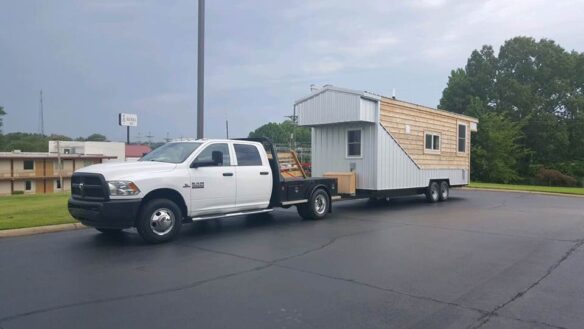 A truck with a trailer attached hauling a tiny house.