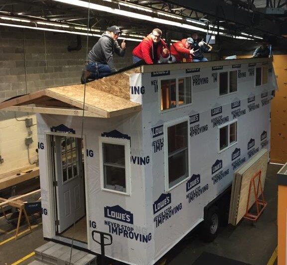 Students work on the roof of a tiny home.