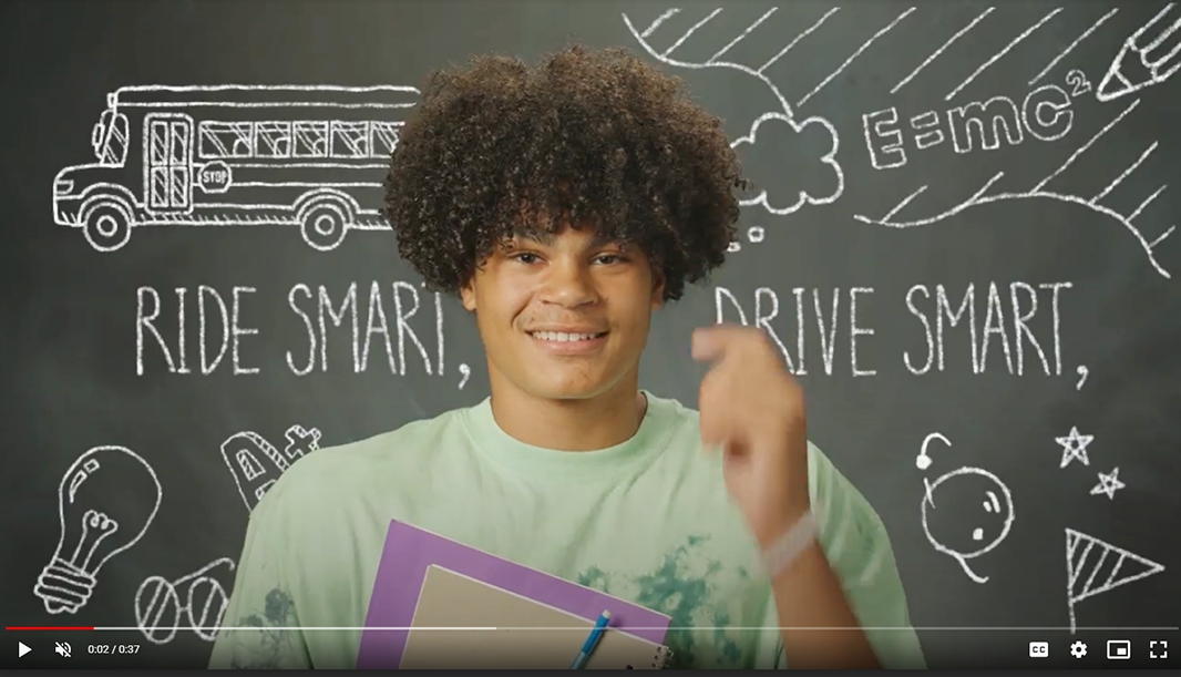Screenshot of a young man in a bus safety video, with line drawings behind him reading Ride Smart, Drive Smart.