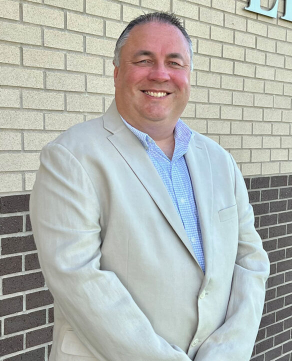 A photo of a man standing in front of a brick wall while smiling. 