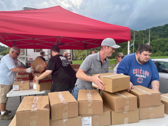 A group of people under a tent moving boxes on a table. 