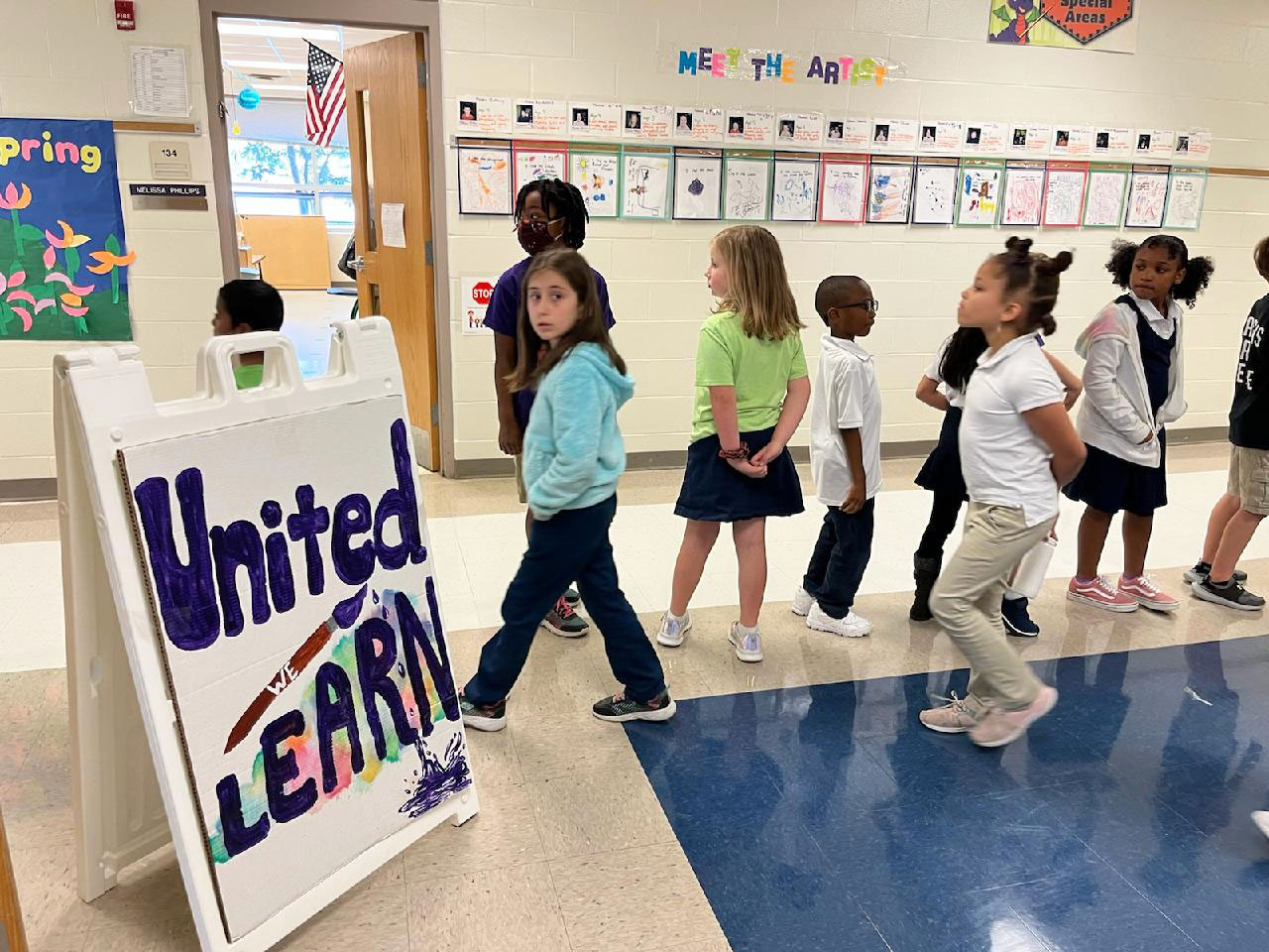 Students walking in a hallway past a sign that reads: "United We Learn"