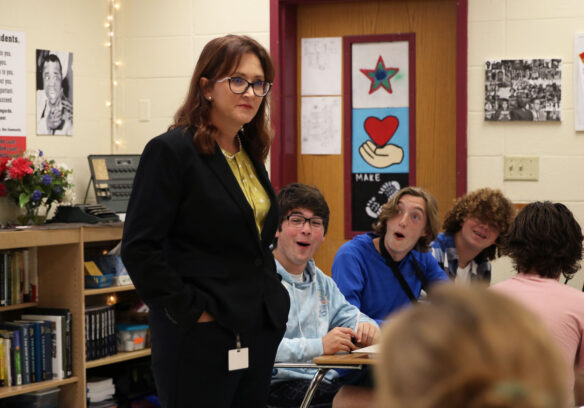 A picture of Amber Sergent standing in her classroom, while all of the students seated around her look surprised and smile.