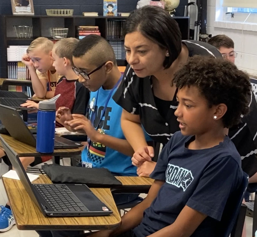 Picture of Mandy Perez looking at a computer over the shoulder of a student in her classroom.