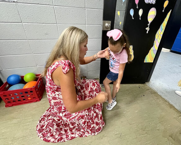 A teacher kneels down to greet a student into the classroom. 