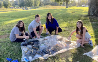 A picture of Kelly Gates sitting under a tree with three young students.