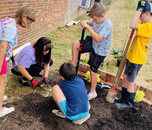 Picture of Kelly Gates digging in the dirt with young children.