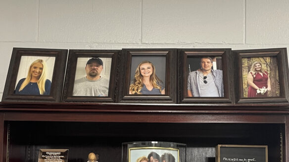 A row of headshot photos in picture frames sitting on top of a bookshelf. 