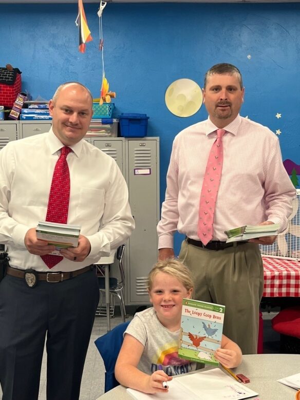 James Cornett poses for a picture with another man and a young girl holding a book and smiling. 