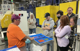 Picture of a woman speaking to a group of students on a factory floor.