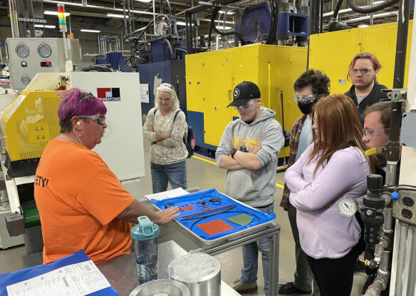Picture of a woman speaking to a group of students on a factory floor.