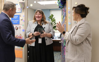 Picture of Jason Glass and Lt. Gov. Jacqueline Coleman surprising Heather LeBlanc with a glass trophy at the door of her office.