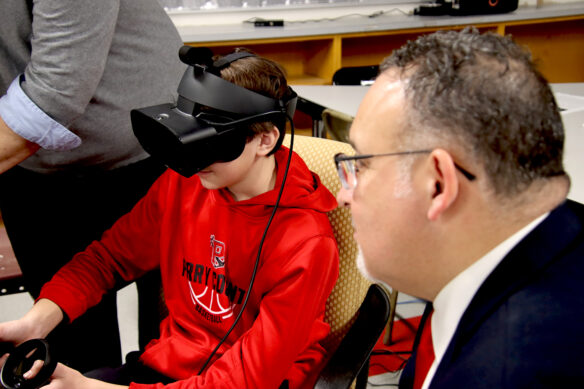 A Perry County High School student wears a virtual-reality headset as he shows U.S. Education Secretary Miguel Cardona what the technology is used for as they sit in a classroom.