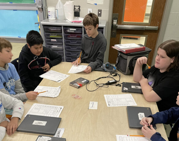 Five students sit around a table looking at Dungeons and Dragons character sheets. 