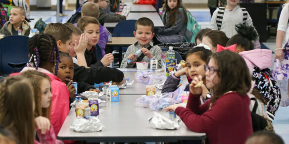 A picture of children eating around the lunch table in the school cafeteria.