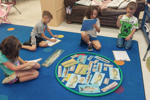 A group of kids sit around pictures of fish