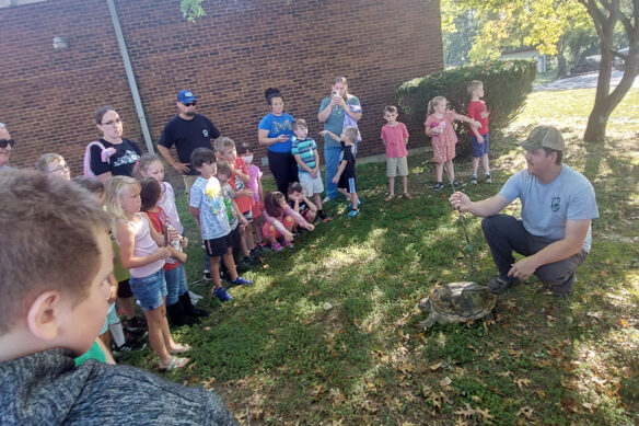 A group of kids circle a man and a turtle