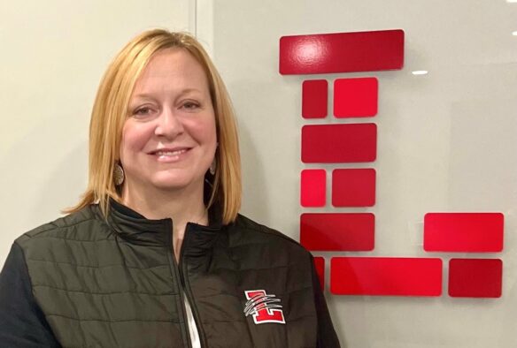 A woman smiles in front of an 'L' sign designed to make it look like it's made of bricks.