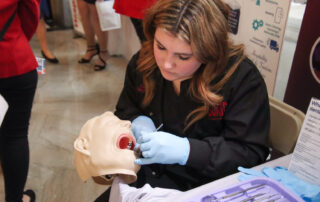 A woman uses dental instruments on a mannequin.