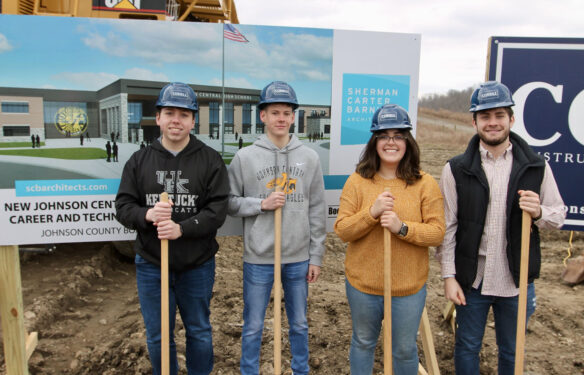 A picture of Johnson Central High School students Brandon Holbrook, Hunter Burchett, Constance Martin and Nick Hardin standing in front of a construction sign and holding on to shovels, wearing construction hats.